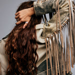 Red-haired model standing with her back to the camera, wearing a stylish jacket against a grey background. Her hand reaches over her shoulder to move her hair, revealing the Ring of Fire Recycled Sterling Silver by Märta Larsson on her thumb. The ring’s bold 11 mm band and flame-inspired design add a striking detail to the dynamic, fashion-forward composition.