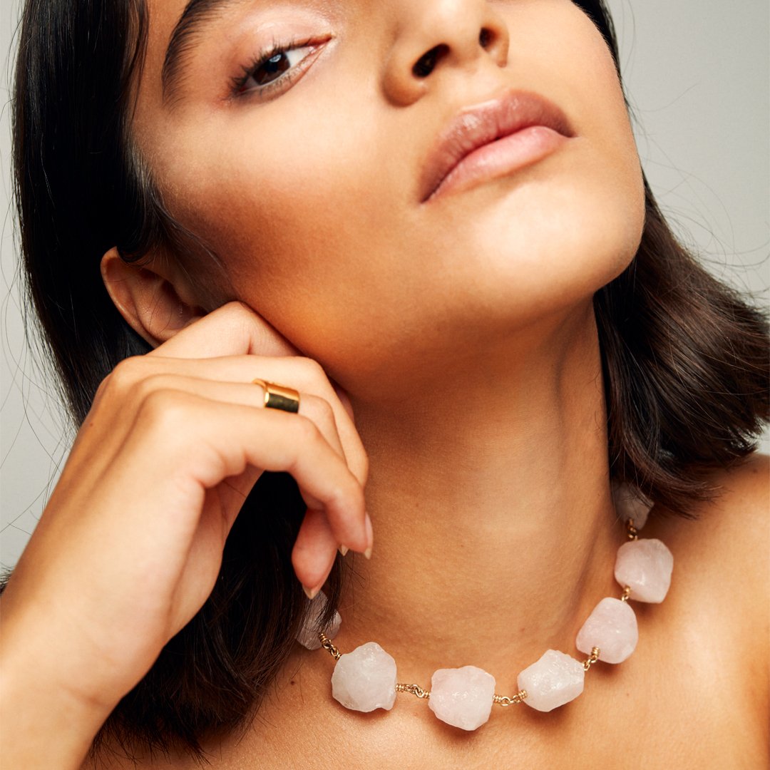 Model touching her ear, wearing the Signature Gold Vermeil Ring by Märta Larsson on the ring finger. The engraved logo and sculptural band make this designer gold ring a timeless accessory in Swedish jewelry.