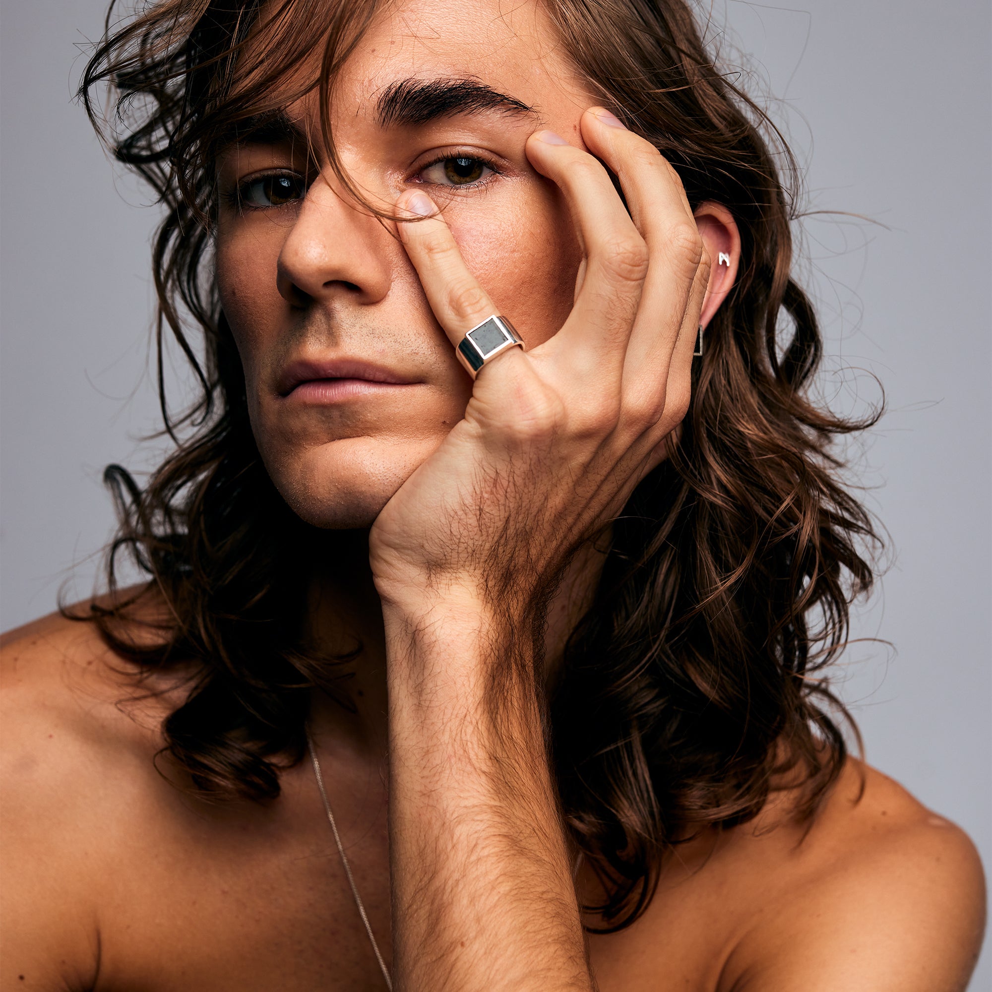 Close-up of a male model wearing the Black Tourmaline Ring by Märta Larsson on his pinky finger, hand near his face. This brushed silver ring with black tourmaline adds a bold statement to any outfit, ideal for lovers of brutalist and crystal jewelry.