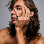 Male model wearing the Black Tourmaline Ring by Märta Larsson on his pinky finger, hand resting on his face. This gold vermeil ring with black tourmaline is a bold accessory for those seeking crystal energy and modern jewelry design.