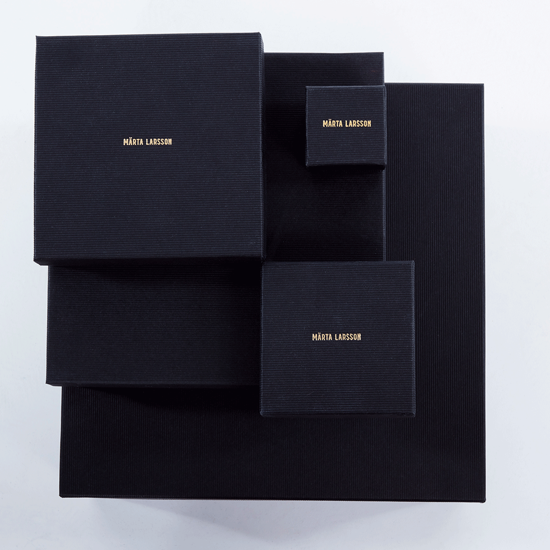 Collection of black jewelry boxes with gold Märta Larsson branding. Elegant packaging for handcrafted gemstone rings and luxury accessories.