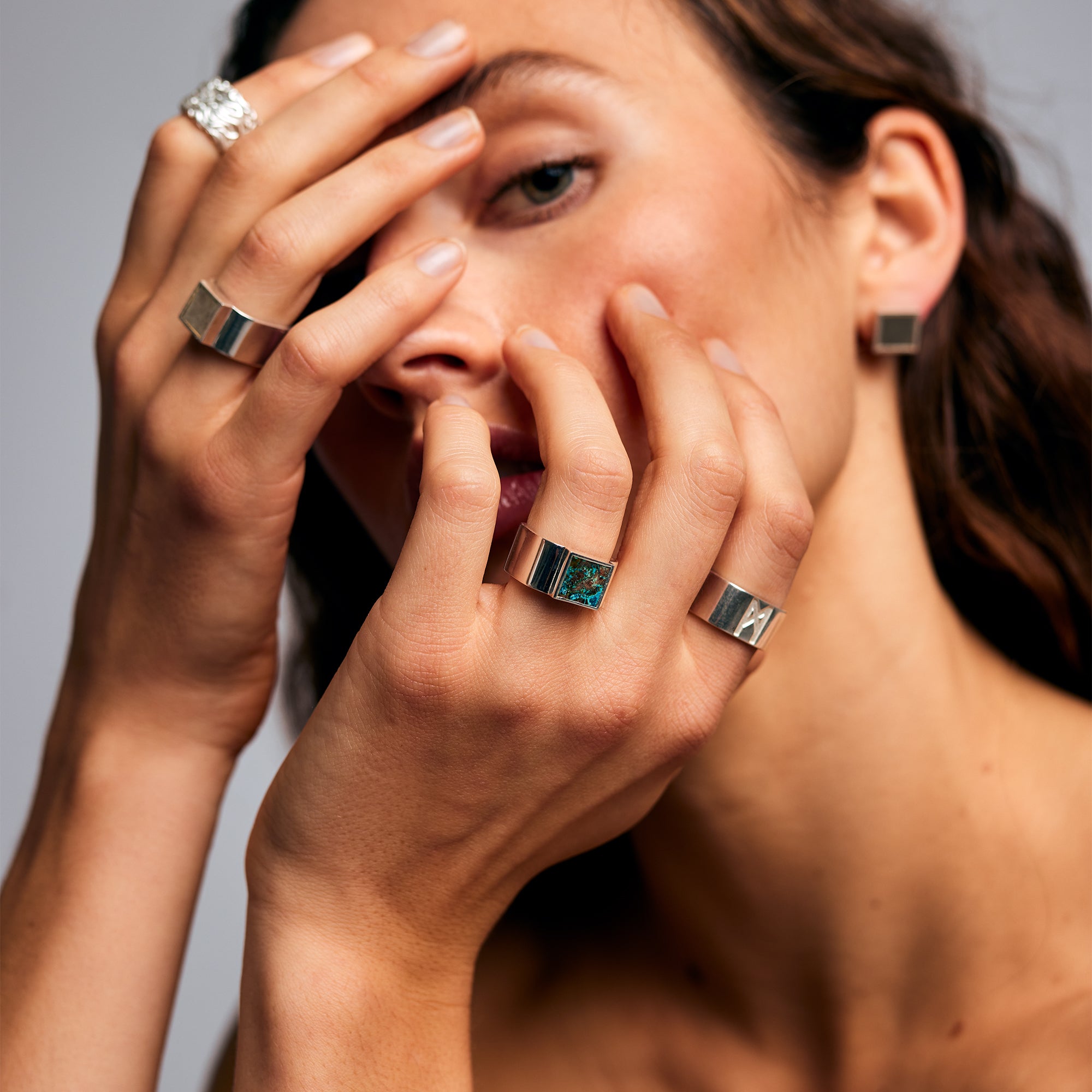 Female model with hands raised over her face wearing the Shattuckite Signet Ring by Märta Larsson on her ring finger. The bold stone and sculptural band make this gemstone ring a modern icon in luxury womens jewelry.