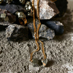 Jewelry styled on volcanic rocks featuring Tie Me Up Pyrite Necklace by Märta Larsson with matching ring and earrings. Raw pyrite crystal necklace styled for rugged elegance and natural power.