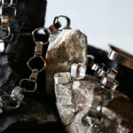 Signature Creole Brushed Silver Earrings by Märta Larsson displayed on dark rocks with other silver jewelry. Brushed silver hoops styled for raw elegance and contrast.