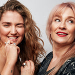 Two women photographed against a grey background. On the left, a brown-haired model wears two Billie Ring Recycled Silver by Märta Larsson, styled with playful expression. On the right, Märta Larsson wears a Billie Ring with red lipstick. A bold silver ring for women that adds personality and elegance to luxury caftan styling and everyday fashion.