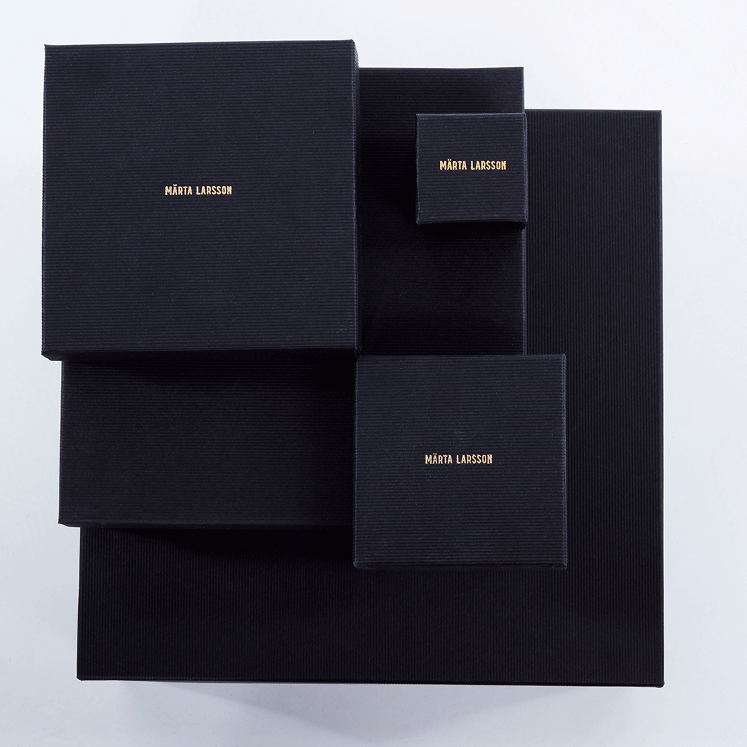 Luxury packaging for Märta Larsson jewelry, black boxes with gold branding designed for pyrite rings and crystal accessories.