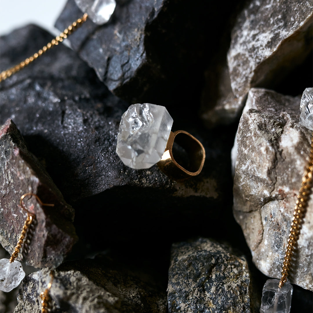 Close-up of quartz ring placed among dark rocks. Roxx Quartz Ring by Märta Larsson with faceted gemstone — contrast between raw nature and refined luxury.