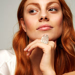 Model with red hair wearing Roxx Quartz Ring by Märta Larsson on right hand. Clear crystal ring styled with satin garment and gold earring — soft and luminous look.