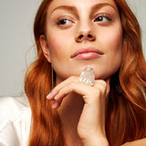 Model with red hair wearing Roxx Quartz Ring by Märta Larsson on right hand. Clear crystal ring styled with satin garment and gold earring — soft and luminous look.