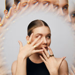 Female model wearing The Billie Ring by Märta Larsson on the middle finger, hands raised over her face. This crystal ring for women blends rawness with elegance, perfect for fashion-forward styling.
