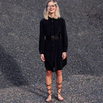 Model wearing the Carte Blanche Silk Shirt Dress by Märta Larsson, standing near a gravel mound with hair partially covering the face. The natural setting and relaxed styling evoke effortless elegance, ideal for luxury shirt dress looks.