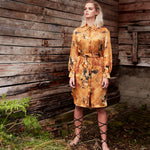 Model wearing the Carte Blanche Silk Satin Shirt Dress by Märta Larsson, standing in front of a wooden plank background. The contrast between the natural texture and the fluid silk fabric enhances the timeless appeal of this designer shirt dress.