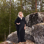 Luxury black silk kaftan dress by Märta Larsson, elegant drape in outdoor forest setting.