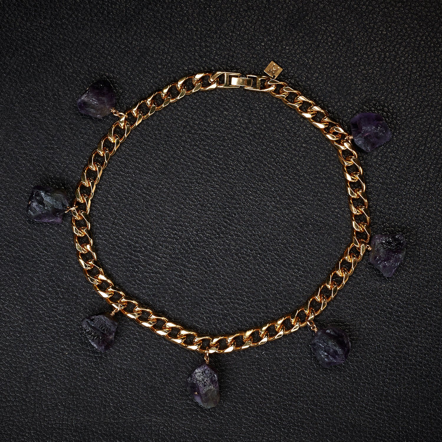 Collar Amethyst Bracelet by Märta Larsson laid out on black textured surface. Gold bracelet with raw amethyst charms — elegant, expressive, and naturally powerful.