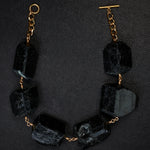 Not A Pearl Necklace XXL Black Tourmaline by Märta Larsson laid out on black textured surface. Chunky black tourmaline necklace with gold toggle clasp — raw elegance meets artisanal power.