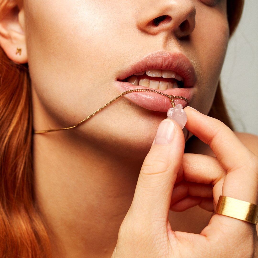 Zoomed-in image of a red-haired model holding a necklace near her lips, wearing the Signature Brushed Gold Ring by Märta Larsson in brushed 24 carat gold vermeil with bold matte band.