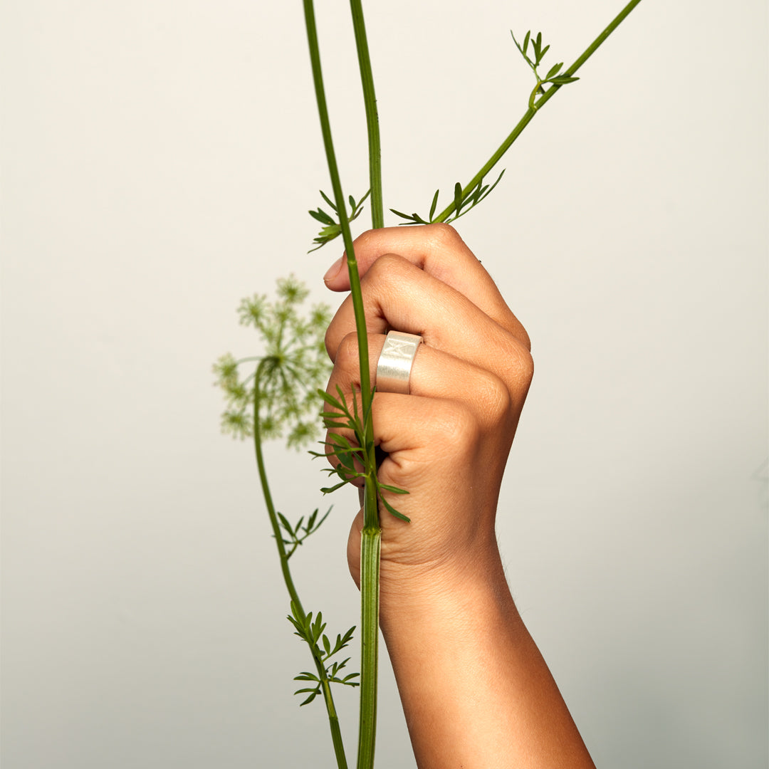  Hand holding green plant stem while wearing brushed silver ring by Märta Larsson, styled with minimalist elegance and natural contrast.