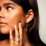  Close-up of brushed silver ring worn with ear cuff and crystal earring, highlighting layered jewelry styling and clean metallic surfaces.