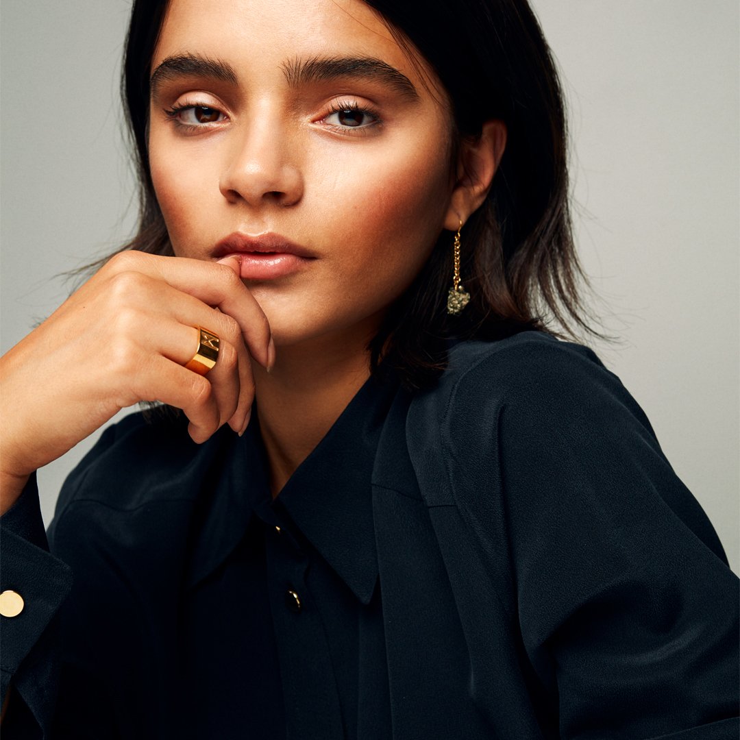Model with hand near mouth wearing the Signature Gold Vermeil Ring by Märta Larsson on the ring finger, a polished refined gold-vermeil statement piece