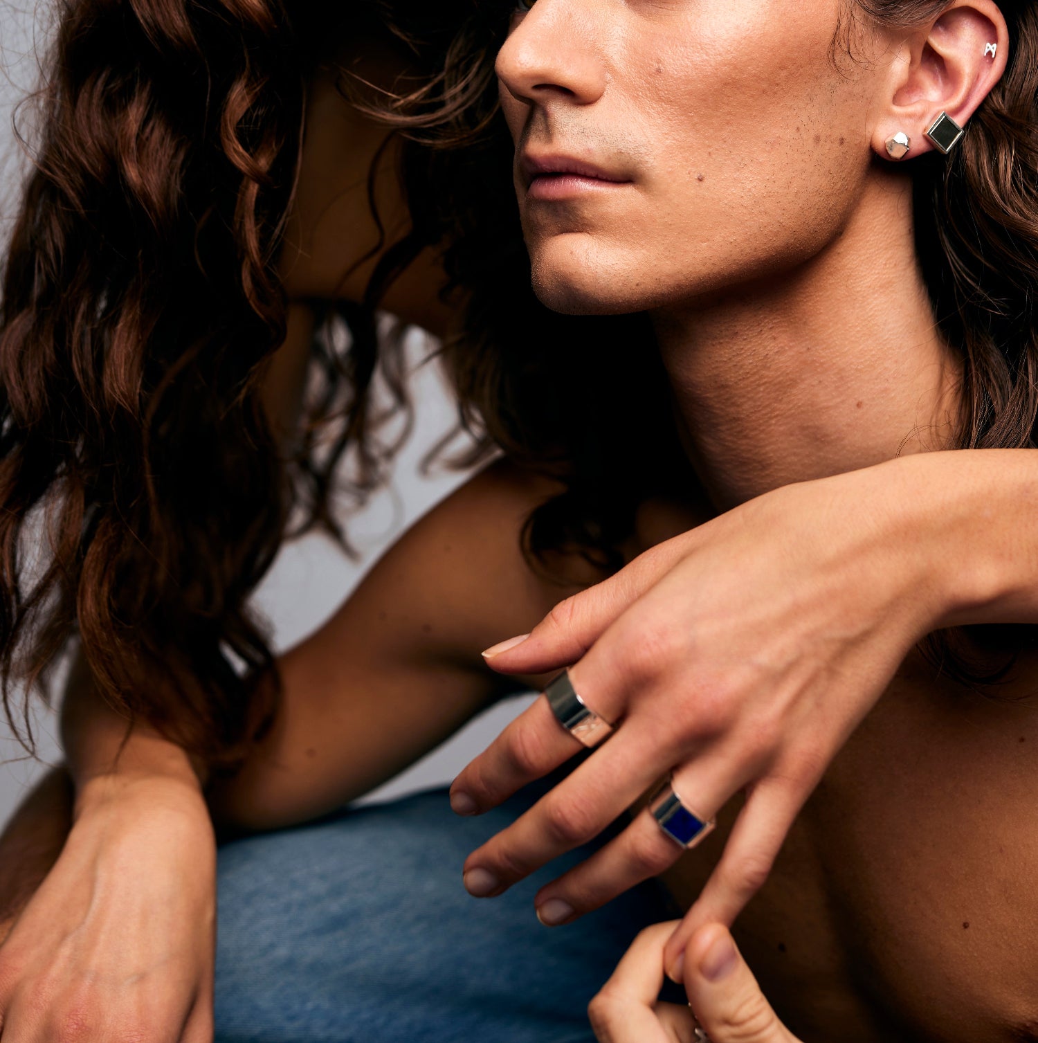 Close-up of two individuals, one wearing the Mondrian Ring Lapis Lazuli by Märta Larsson with square earring and layered rings, an artistic display of modern gemstone jewelry.
