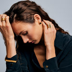  Model in dark shirt wearing the Mondrian Ring Ruby Zoisite by Märta Larsson with gold jewelry. Wide gold ring with green stone styled alongside geometric earrings and bracelet.