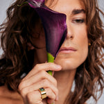 Model holding a dark purple calla lily in front of face, wearing the Mondrian Ring Ruby Zoisite by Märta Larsson on ring finger. Artistic gold ring with green and black stone, styled with floral contrast.
