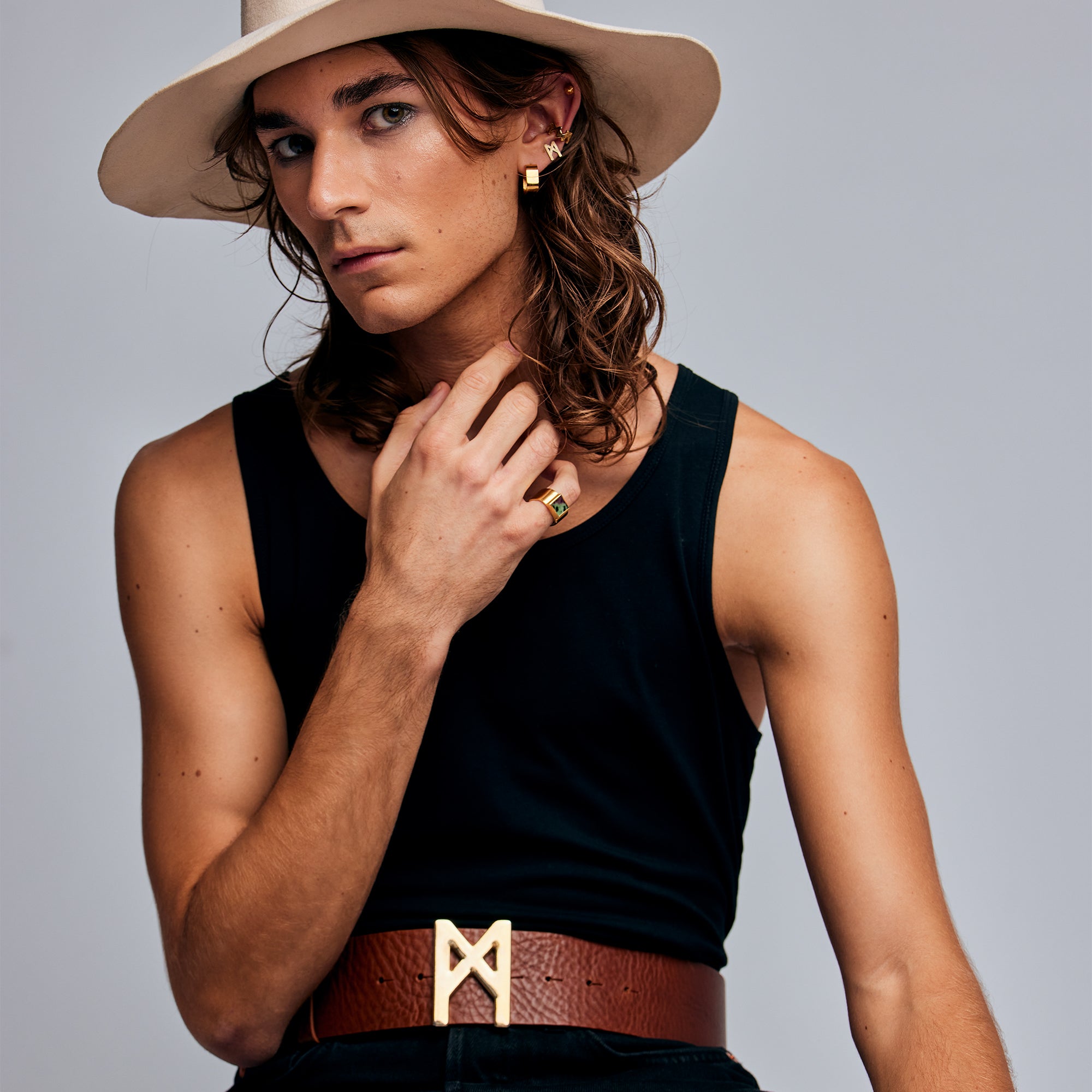 Model in beige hat and black top wearing the Mondrian Ring Ruby Zoisite by Märta Larsson. Gold jewelry styled with rune-like belt buckle and square ear cuff.