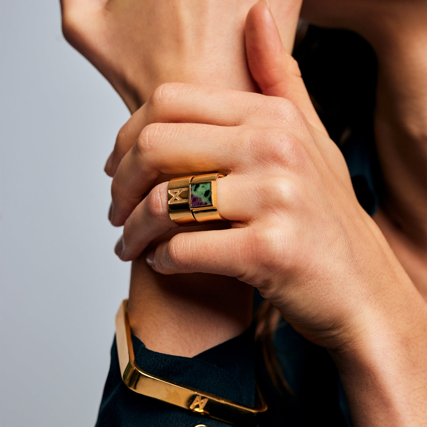Close-up of hands with gold jewelry featuring the Mondrian Ring Ruby Zoisite by Märta Larsson on the index finger, a sculptural gold-vermeil ring with vibrant natural stone.