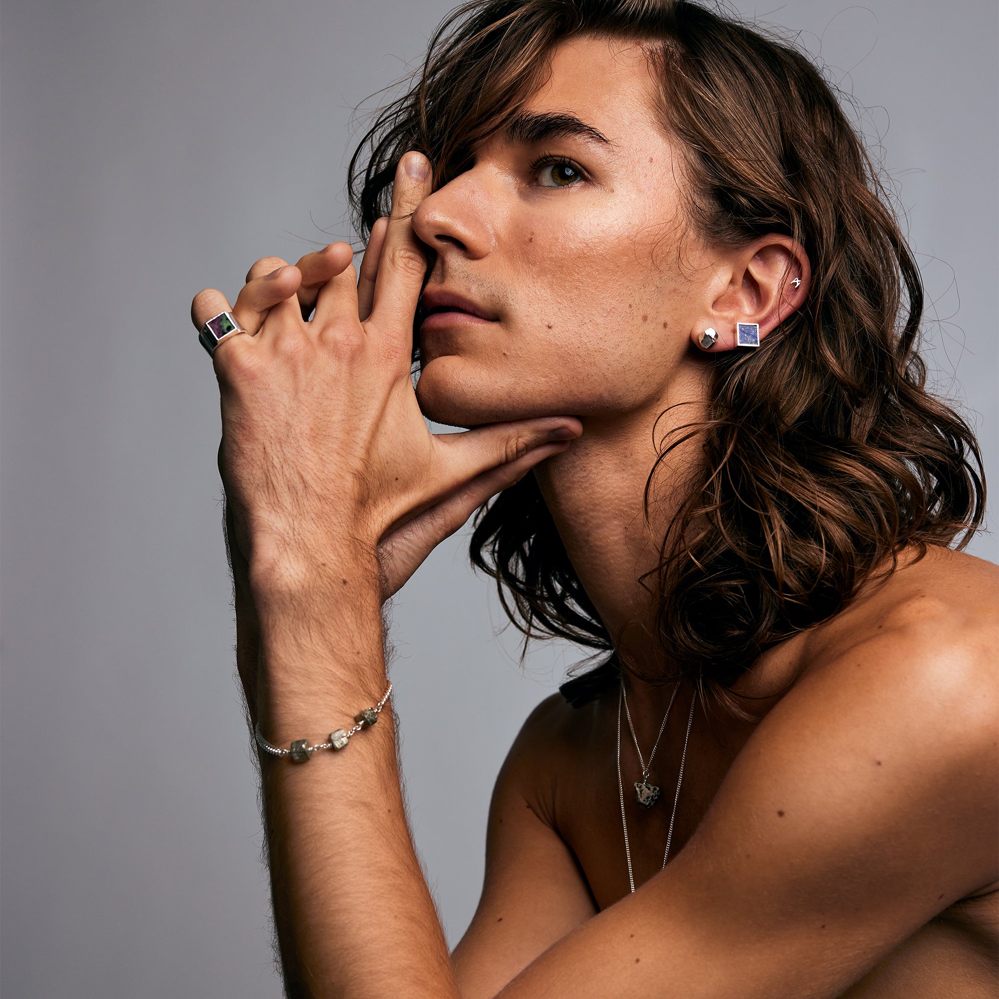 Model with layered jewelry wearing the Mondrian Ring Ruby Zoisite by Märta Larsson on the left hand. Artistic composition with silver ring, butterfly pendant, and square earrings.