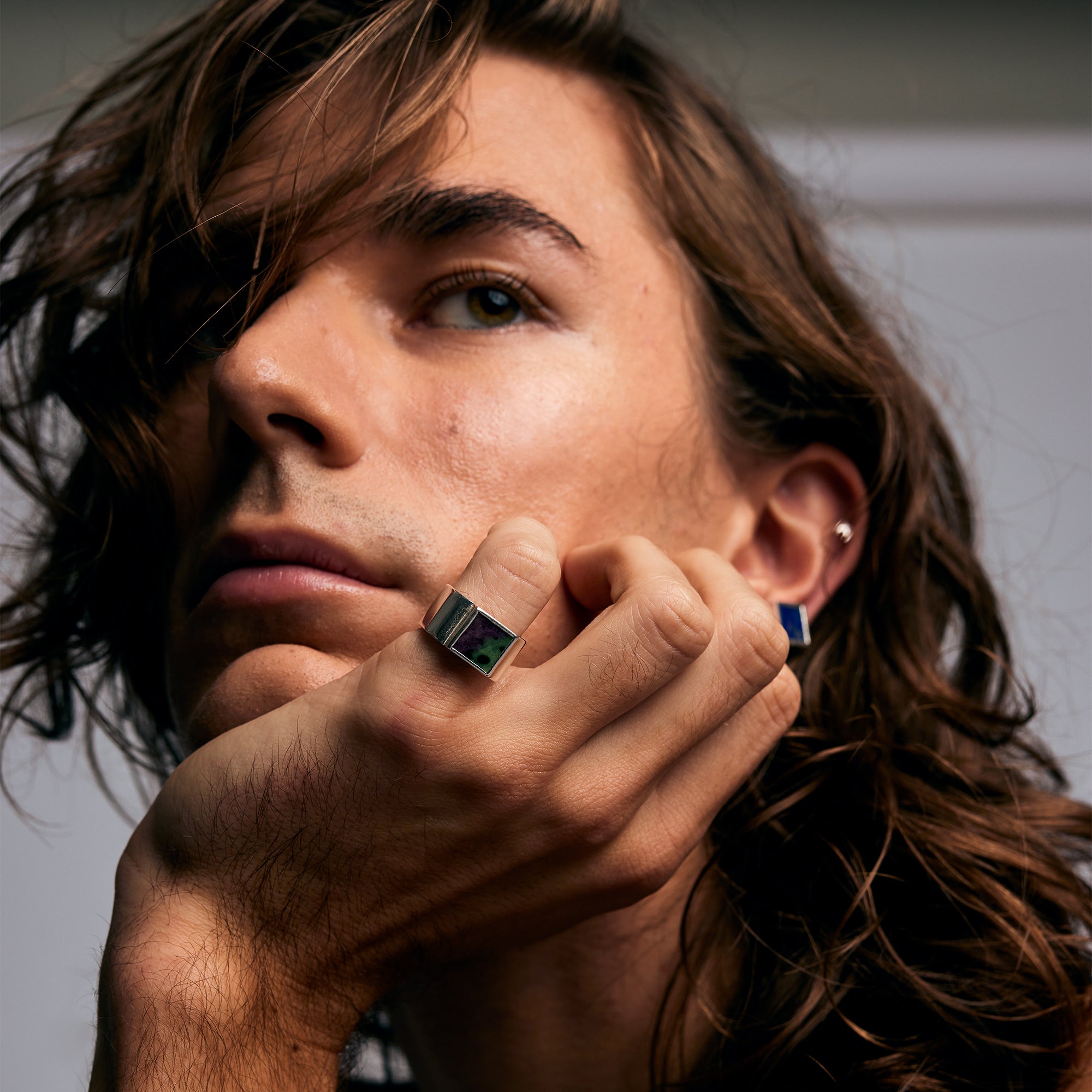 Model resting chin on hand wearing the Mondrian Ring Ruby Zoisite by Märta Larsson on index finger. Silver ring with green and black stone, styled with blue accent ring and soft lighting.