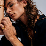 Model in dark shirt with gold buttons wearing the Mondrian Ring Garnet in Limestone by Märta Larsson on the ring finger, a layered gold look highlighting its sculptural elegance.