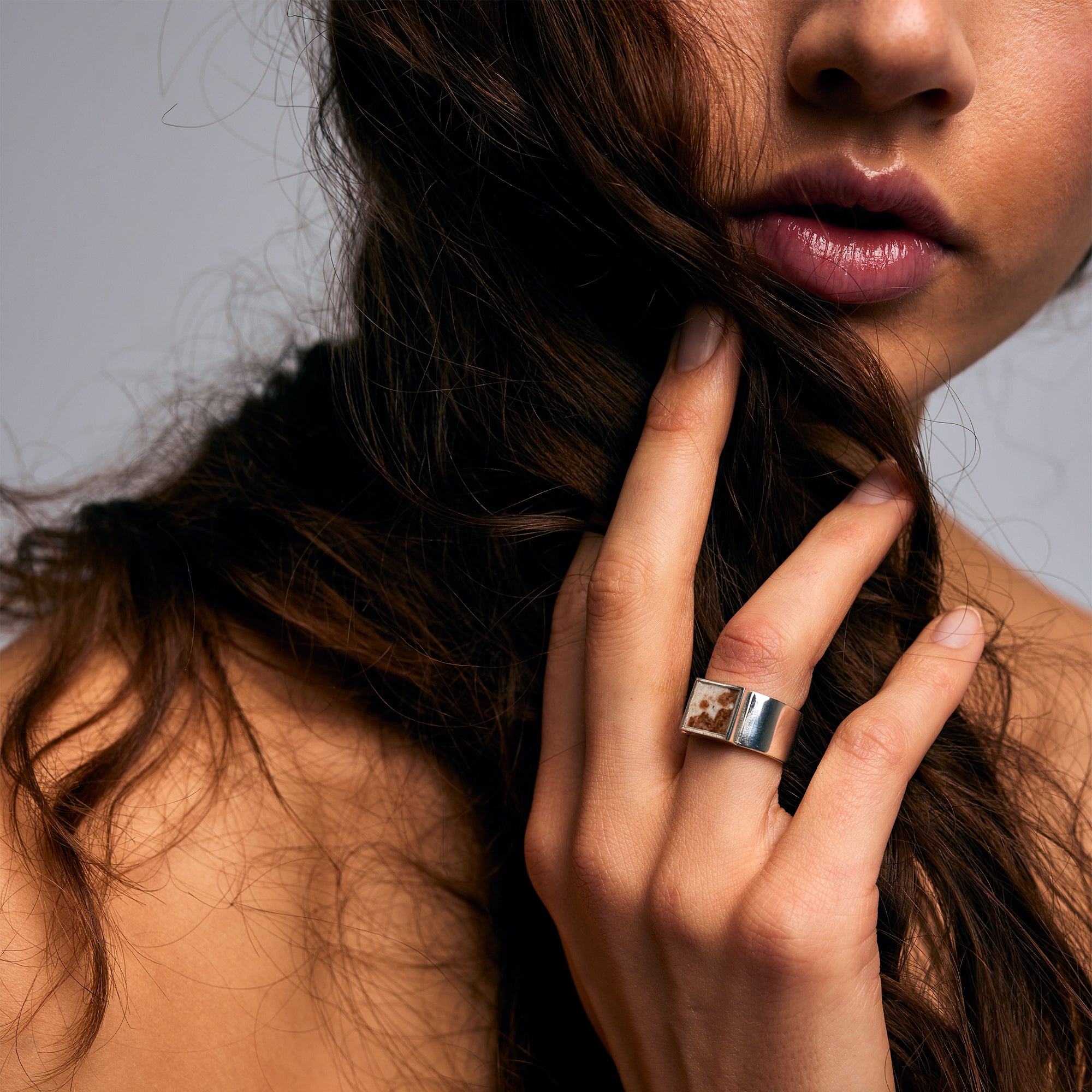 Close-up of a person holding their hair wearing the Mondrian Ring Garnet in Limestone by Märta Larsson on the middle finger, an artistic gold-vermeil gemstone ring with earthy stone detail.