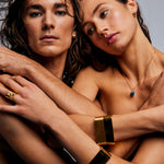 Two models posed together with one wearing the Mondrian Ring Garnet in Limestone by Märta Larsson, an artistic gold jewelry composition with intertwined arms.