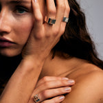 Model resting her hand against her cheek, wearing the Mondrian Ring Pyrite by Märta Larsson with square-cut pyrite stone and recycled silver band, showcasing bold modern elegance.