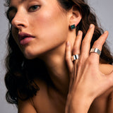 Brown-haired model posing against a grey background, wearing the Mondrian Ring Pyrite by Märta Larsson on her index finger with 9x9 mm square-cut pyrite stone and recycled silver setting.    