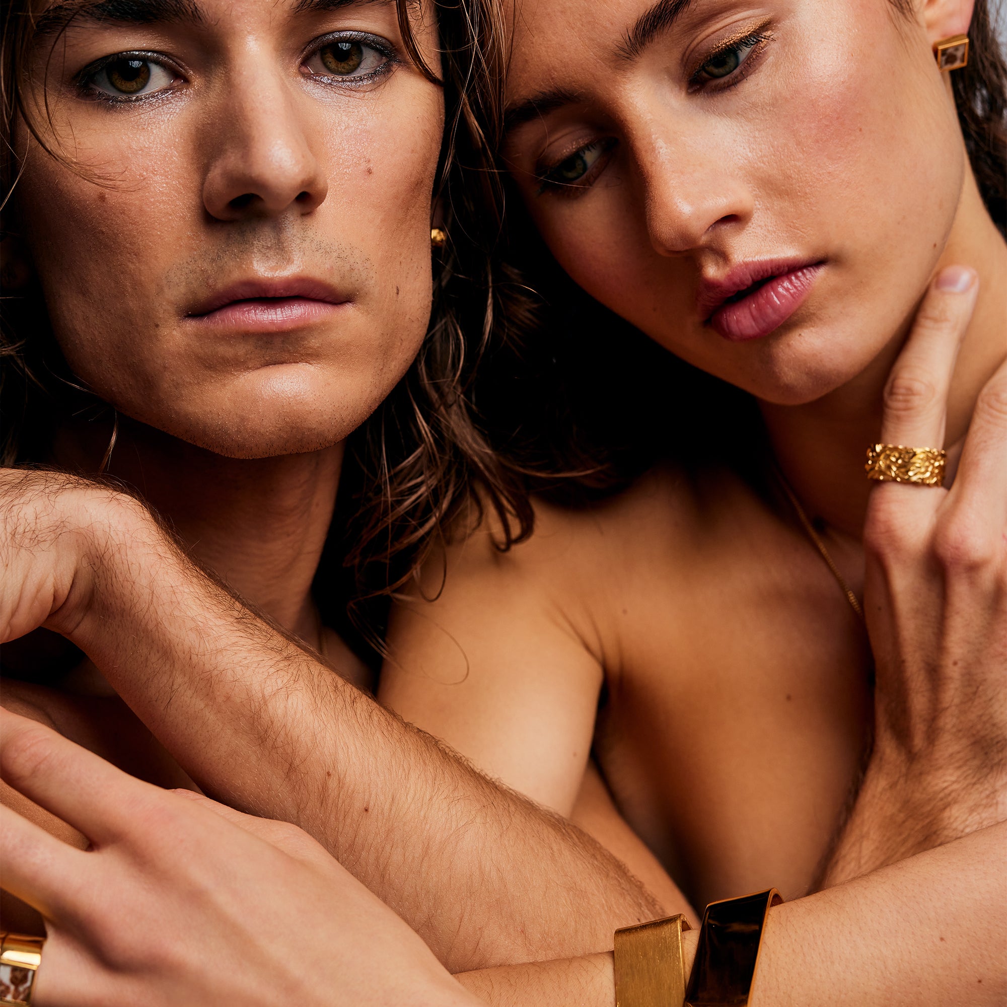 Male and female models posing, with the male wearing the Ring of Fire Gold by Märta Larsson on the pinky, a unisex sculptural gold-vermeil statement ring.