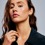 Female model with hand near neck wearing the Ring of Fire Gold by Märta Larsson on the ring finger, a sculptural gold-vermeil ring with engraved detail.