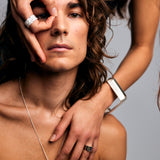 Male model with a female model behind him, her hand forming an “O” over his eye while wearing the Ring of Fire Recycled Sterling Silver by Märta Larsson with bold 11 mm flame-detailed band.
