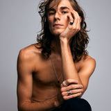 Male model sitting shirtless against a grey background, wearing the Ring of Fire Recycled Sterling Silver by Märta Larsson with bold 11 mm flame-detailed band on his left index finger.