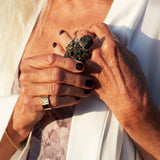 Two hands touching, one wearing the Signature Silver Ring by Märta Larsson on the pinky finger, featuring a polished sculptural silver band with engraved detail.