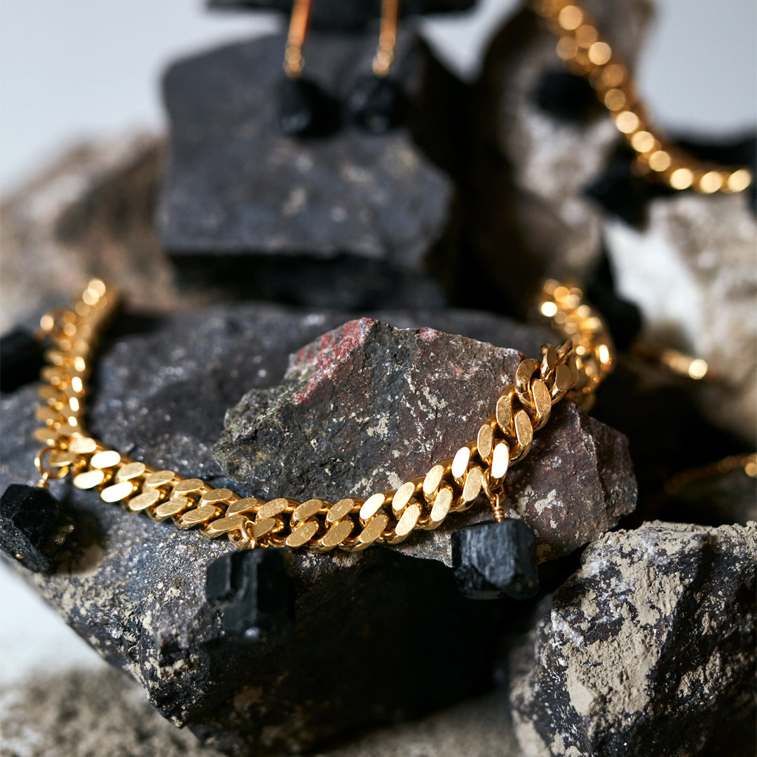 Collar Black Tourmaline Necklace by Märta Larsson on textured rocks, a gold-chain design with raw black tourmaline for bold natural luxury.