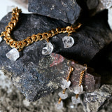 Close-up of the Collar Rough Quartz Necklace by Märta Larsson, a chunky gold chain with raw clear quartz charms styled against textured rocks.