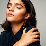  Gold vermeil logo ring worn with dark shirt and green bead earring, showcasing sculptural jewelry styling and confident expression.