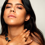 Model with long black hair photographed against a grey background, wearing the MMM Polished Gold Vermeil Ring by Märta Larsson with polished gold surface and repeating “M” logo detail.