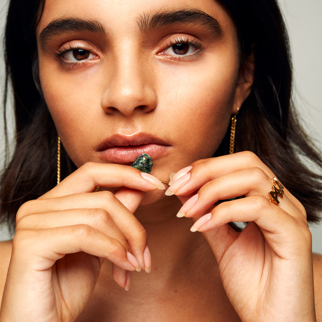 Close-up of a brown-haired model wearing the MMM Polished Gold Vermeil Ring by Märta Larsson with polished 24 carat gold finish and bold repeating “M” logo in soft expressive lighting.