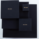 Product packaging for Märta Larsson displayed against a grey background with black boxes of varying sizes and gold lettering, highlighting luxury craftsmanship and refined presentation.
