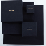 Product packaging for Märta Larsson displayed against a grey background with black boxes of varying sizes and gold lettering, highlighting luxury craftsmanship and refined presentation.