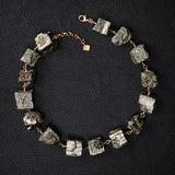 Not a Pearl Necklace Pyrite by Märta Larsson laid out on a black textured surface, featuring raw pyrite stones on a gold chain.