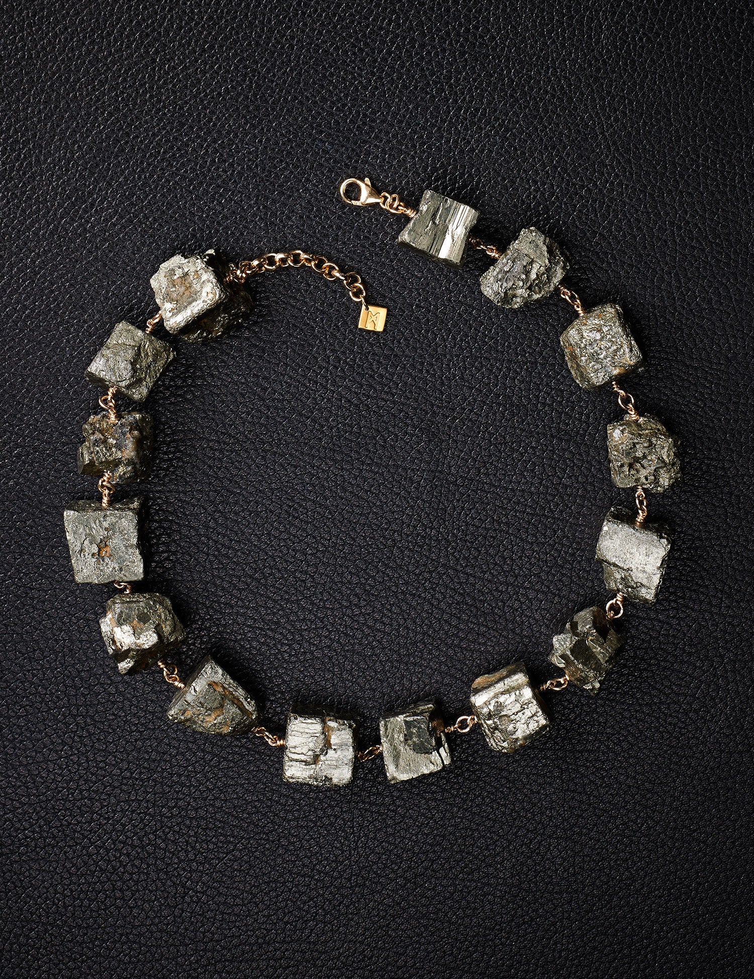 Not a Pearl Necklace Pyrite by Märta Larsson laid out on a black textured surface, featuring raw pyrite stones on a gold chain.