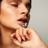 Close-up of model wearing Roxx Pyrite Cube Ring by Märta Larsson on index finger. Pyrite stone ring styled with glowing skin and minimalist makeup — perfect for brutalist fashion.